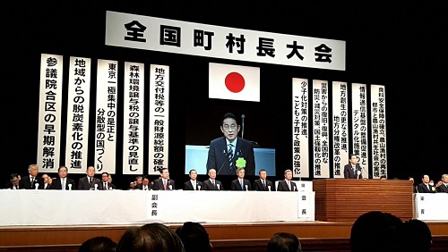 会場に掲げられたスローガンの前で挨拶する岸田首相